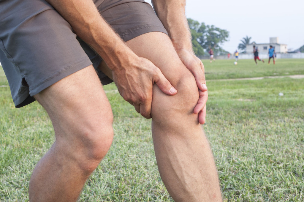 30122550 - closeup of athletic caucasian man holding his painful knee on soccer field
